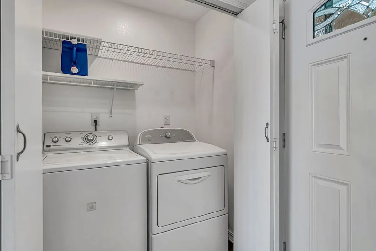 A tidy laundry area equipped with a washing machine, dryer, and shelving organized with laundry supplies. The space is clean and practical, emphasizing convenience for guests staying longer.