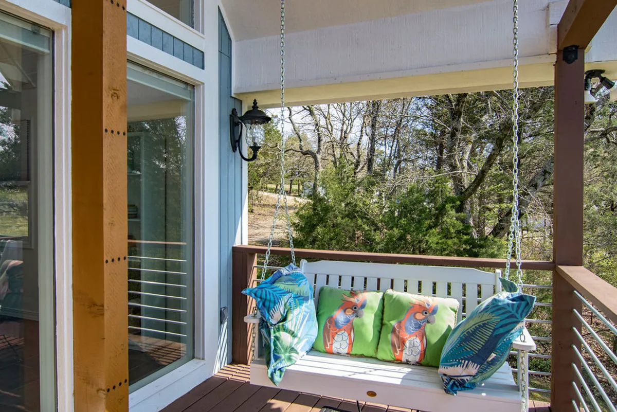 A cozy exterior space featuring a swing with colorful cushions, a lantern light fixture, and abundant greenery around. The scene evokes comfort and relaxation in a lush, natural setting that would appeal to pet owners.