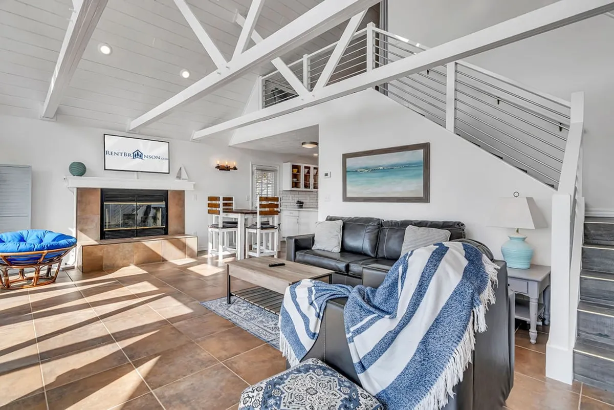 A stylish, contemporary interior with a fireplace, sofa, blue chair, dining area, and artwork. The setting is cozy and set up for relaxing, socializing, and watching TV, with an inviting modern design.