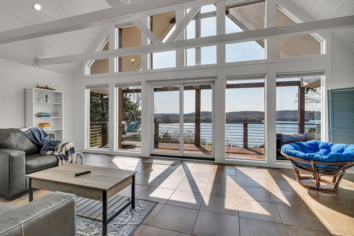 A cozy living room with comfortable seating arranged around a stylish coffee table. Floor-to-ceiling windows offer breathtaking views of the lake, and a decorative bookshelf adds a touch of personality. The space feels tranquil and inviting, ideal for unwinding with a book or enjoying conversation with family and friends.