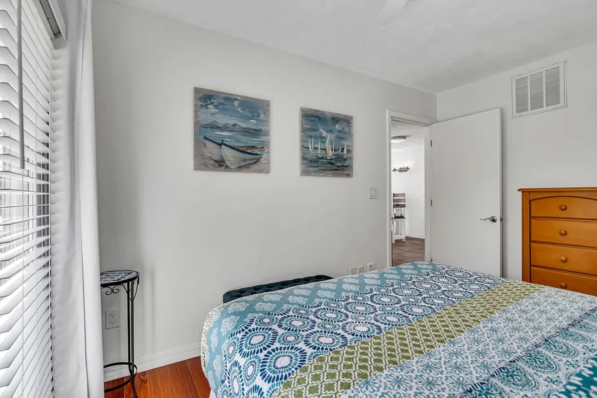 A bedroom with colorful patterned bedding and nautical-themed artwork above a wooden dresser creates a peaceful and inviting space for relaxation and rest.