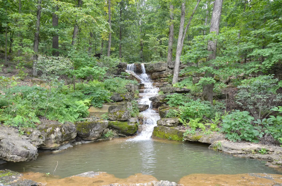 A picturesque outdoor view of a natural waterfall surrounded by lush greenery and rock formations. The scene captures a unique and beautiful seasonal feature of the property, inviting moments of reflection and appreciation for nature.