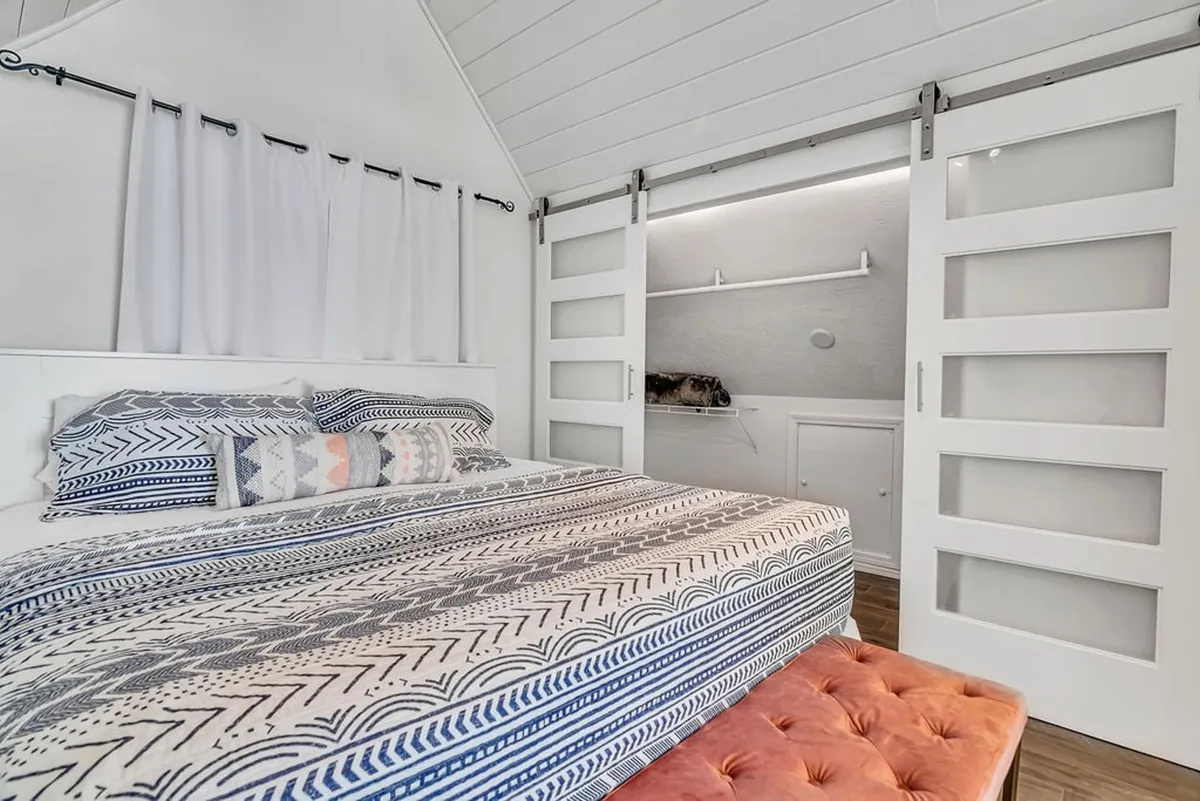 A serene bedroom featuring a bed with patterned bedding and colorful accent pillows sits adjacent to sliding glass doors, allowing natural light to fill the space.