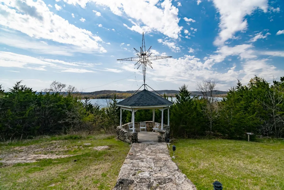 An exterior view featuring a charming gazebo overlooking the water, surrounded by lush greenery. The setting is peaceful and ideal for relaxing, gathering, or stargazing, with beautiful sunset views over the lake.