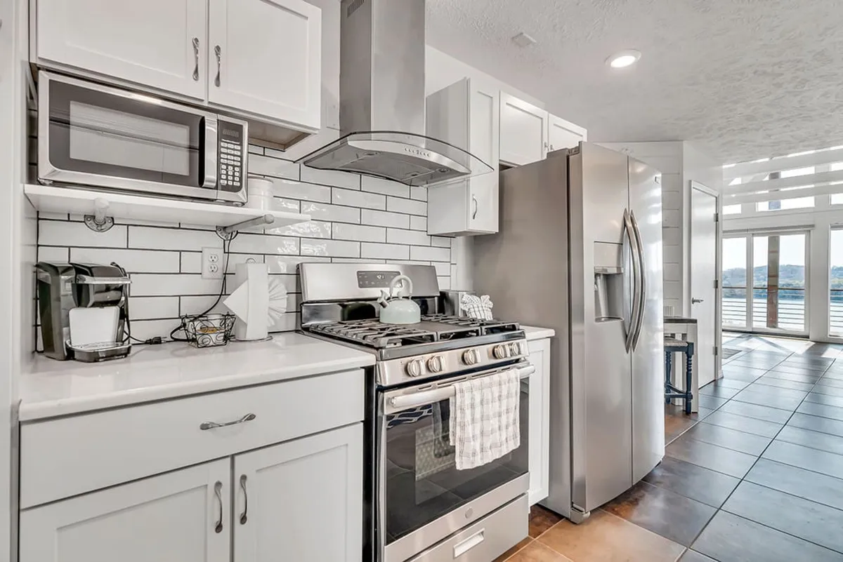 A modern kitchen with stainless steel appliances, white cabinetry, and a central island with seating. Large windows provide another perspective of the water, bringing natural light deep into the space. The kitchen is both functional and inviting, perfect for preparing meals while staying connected to the main living area.